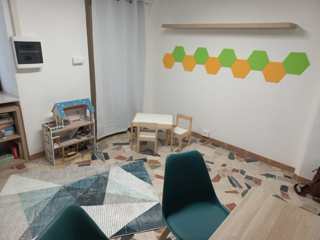 Spazio di psicologia per bambini a Bussoleno, con tavolino, sedie in legno, tappeto colorato e giochi educativi.